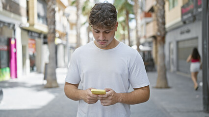 Young, handsome hispanic man, with a serious expression, engrossed in typing a message on his...