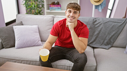 Obraz premium At home, a confident young hispanic man enjoys a morning cup of coffee, comfortably relaxed on the sofa. his handsome expression radiating positivity and joy from his infectious, heartwarming smile.