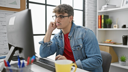 Young hispanic man business worker using computer thinking at the office