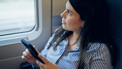 Young beautiful hispanic woman using smartphone sitting inside train wagon - obrazy, fototapety, plakaty