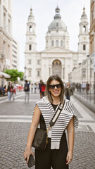 Smiling young woman with sunglasses in front of st stephen's basilica, budapest, showcasing urban european lifestyle.