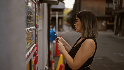 Beautiful hispanic woman with glasses uses phone to buy from kyoto's street vending machine, fusing traditional city charm and modern convenience - obrazy, fototapety, plakaty