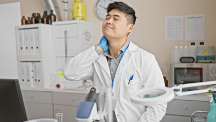 A young asian man in a white lab coat appears tired or stressed in a clinical laboratory setting.