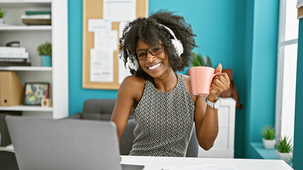 African american woman business worker listening to music drinking coffee at the office
