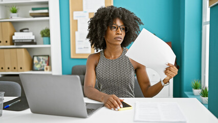 African american woman business worker using laptop using documents as a handfan at the office