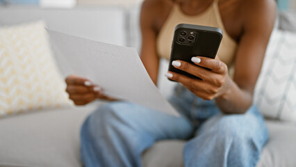 African american woman using smartphone reading document at home