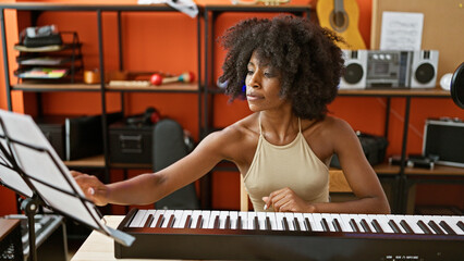 African american woman musician playing piano reading music sheet at music studio