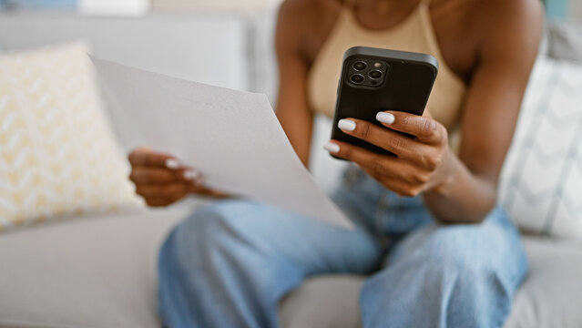 African American Woman Using Smartphone Reading Document At Home