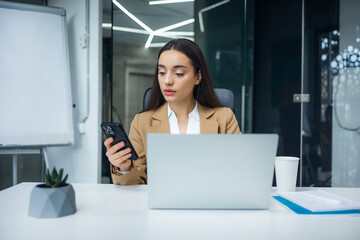 woman sit at workplace desk hold cellphone, synchronize data between computer and gadget in office,...