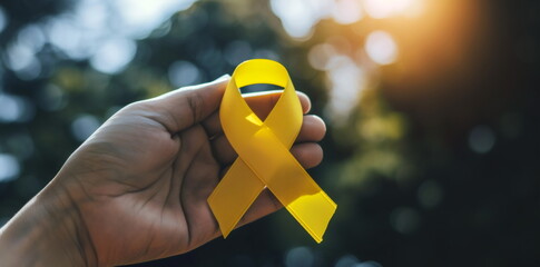 Yellow ribbon in hand. World cancer day, International Childhood Cancer Day, Cancer awareness concept. Suicide prevention day, Sarcoma, bone and bladder cancer Awareness month. For banner