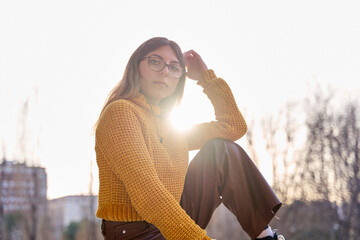 young teenage girl with glasses looking at camera sitting outside with the sun shining in the...
