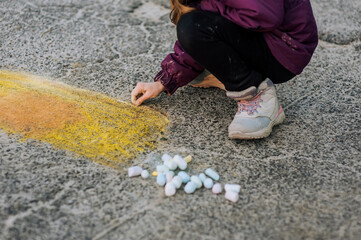 A diligent girl, a child draws a drawing with colored chalk on the asphalt with his hand on the street in a park in Ukraine. Close-up photography, design, childhood concept.