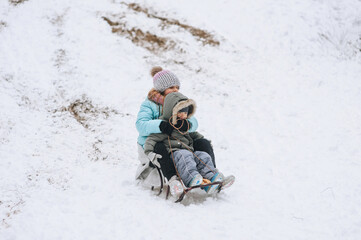 Fototapeta na wymiar A little boy with his sister's girl, happy children, a family, sitting together on a sled, going down a hill in the snow in winter. Photography, portrait, childhood concept, lifestyle.