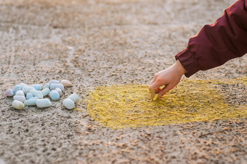 A diligent girl, a child draws a drawing with colored chalk on the asphalt with his hand on the street in a park in Ukraine. Close-up photography, design, childhood concept.
