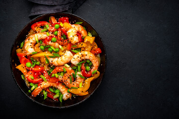 Hot stir fry shrimps with colorful paprika, green peas, chives and sesame seeds with ginger, garlic and soy sauce.   Black kitchen table background, top view