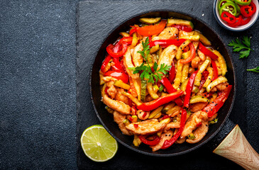 Stir fry turkey breast with red paprika and zucchini with sesame seeds, garlic, ginger and soy sauce in frying pan. Black table background, top view