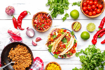 Tacos with ground beef, sweet corn, red beans, tomato salsa sauce and red onion in corn tortillas on plate. Mexican cuisine. Taco party menu. White table background, top view