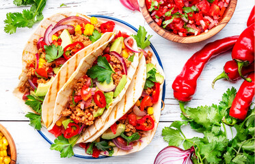 Tacos with ground beef, sweet corn, red beans, tomato salsa sauce and red onion in corn tortillas on plate. Mexican cuisine. Taco party menu. White table background, top view