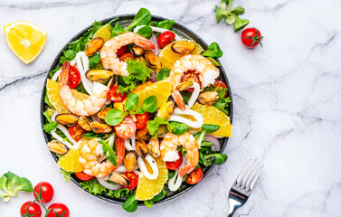 Delicious salad with seafood, oranges, lamb lettuce and olive oil with lemon juice dressing, marble table background, top view