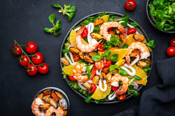 Delicious salad with shrimp, mussels, squid, oranges, lamb lettuce and olive oil with lemon juice dressing, black table background, top view