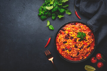 Chili con carne, mexican dish with minced beef, red beans, paprika, corn, cilantro and red peppers in spicy tomato sauce, tex-mex cuisine, black table background, top view