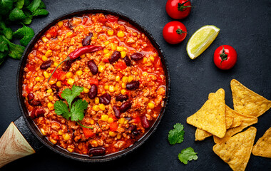 Chili con carne, mexican dish with minced beef, red beans, paprika, corn, cilantro and red peppers in spicy tomato sauce, tex-mex cuisine, black table background, top view