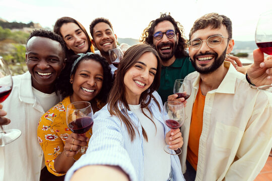 Happy young friends taking selfie group together enjoying summer party. Millennial people having fun toasting red wine at rooftop celebration - Powered by Adobe