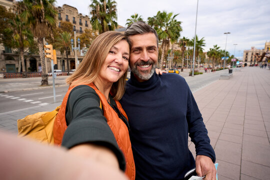 Happy Caucasian middle-aged tourist couple take selfie together. Husband and wife love smiling looking at frontal camera enjoying journeys in European city street. Adult people romantic sightseeing 