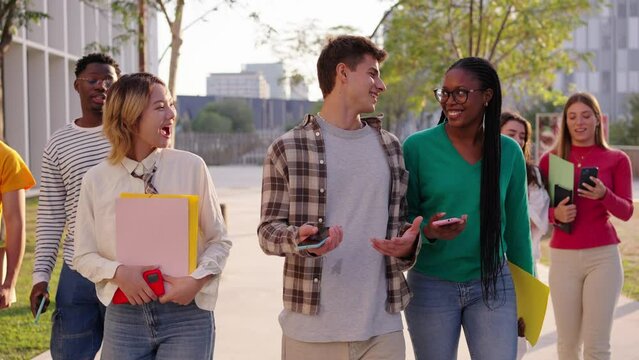 A large multiracial group of teenagers laughing and having fun walking together in an outdoor university campus. Young students enjoying their leisure and free time with friends in the park
