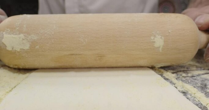 Chef rolls out the dough. Close up of male hands with rolling pin rolling out the dough