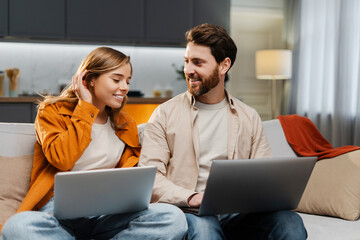 Portrait of smiling man and woman, freelancers sitting on comfortable sofa, in co-working or at home, working, online shopping, using laptop, website. Teamwork concept