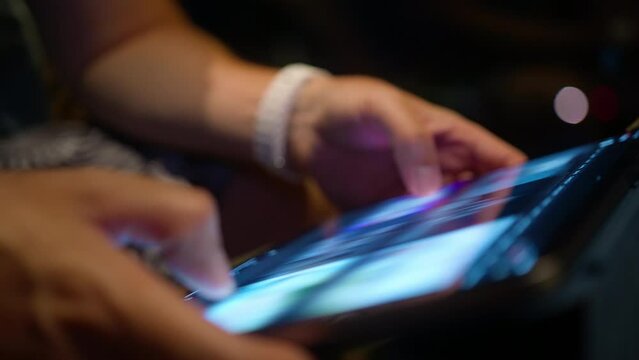Closeup male hands searching on tablet screen, browsing videos or image content using WiFi at night. Close view modern tech device bright screen. Young man scrolling content online, wireless internet