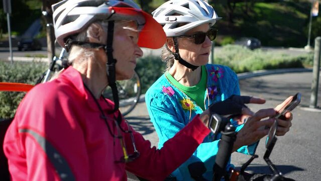 Closeup of senior and mature woman take a break while biking to look at a map on their phone for directions.