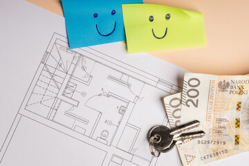 colorful cards with smiling faces drawn, next to them there is a technical drawing of an apartment, door keys and Polish PLN banknotes