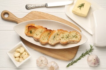 Tasty baguette with garlic and dill served on white wooden table, flat lay