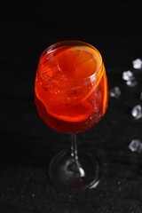 Glass of tasty Aperol spritz cocktail with ice cubes on table against black background