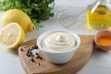 Tasty mayonnaise sauce in bowl, ingredients and spices on white table, closeup
