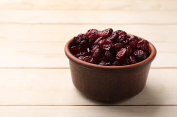 Tasty dried cranberries in bowl on light wooden table, closeup. Space for text