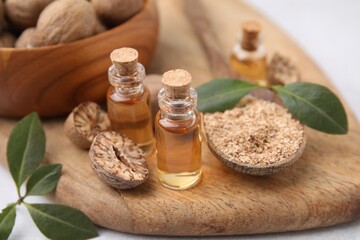 Nutmeg essential oil, whole and ground nuts on wooden board, closeup