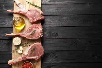 Fresh tomahawk beef cuts, spices and oil on black wooden table, top view. Space for text