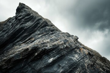 The jagged rock face stands imposingly against the brooding sky, its layers telling stories of ancient geological events etched by time.