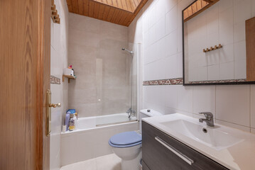 A small bathroom with white porcelain toilets on dark wooden furniture, a framed mirror on the wall and tiles with a half-height border