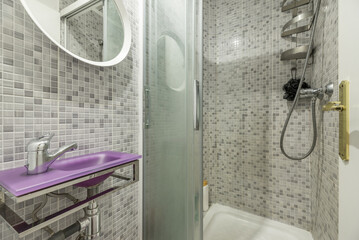 A small bathroom with fuchsia tinted glass sink, beneath a white circular mirror