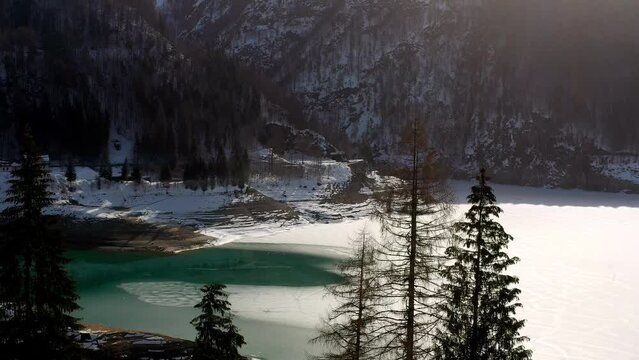 drone flying over a frozen valley in the mountains covered by snow with a river and a lake