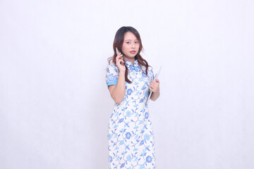 Beautiful Indonesian Chinese woman looking at the camera wearing a modern Chinese blue dress holding a tablet while making a phone call isolated on a white background