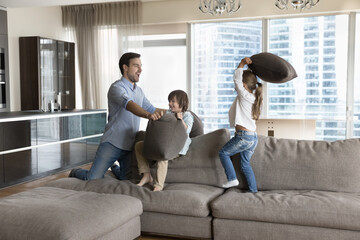 Cute crazy kids spend time with young daddy in living room, have fun together, fighting with...