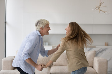Fototapeta premium Joyful excited adult child and active senior father training energetic social dance at home together, having fun, enjoying family leisure time, active hobby, laughing, moving