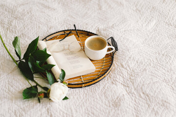 Still life details in home interior of living room. Open book with glasses, cup coffee and bouquet white pink peonies flowers. Read and rest. Cozy home