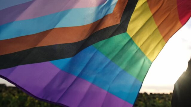 Rainbow LGBTQIA flag waving in wind made from silk material on field background. Symbol of LGBTQ pride month. Equal rights. Peace and freedom concept