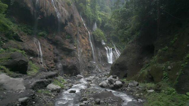 Aerial flies down narrow river canyon with waterfalls on cliff walls